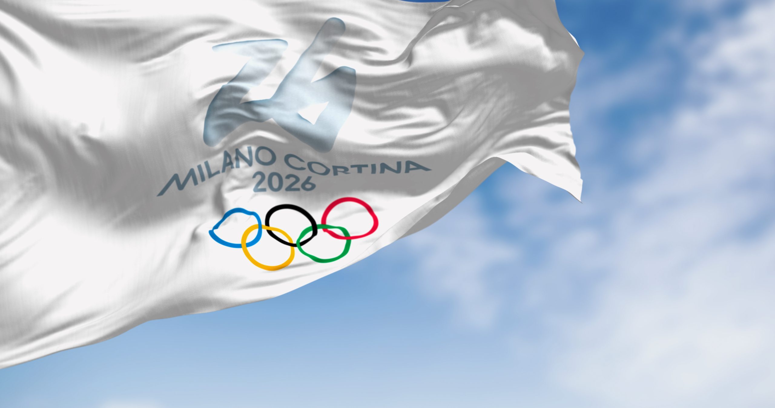 Powiewająca flaga Milano Cortina 2026 z logo olimpijskim – ilustracja artykułu o roli Zimowych Igrzysk Olimpijskich w walce z suszą i zmianą klimatu.